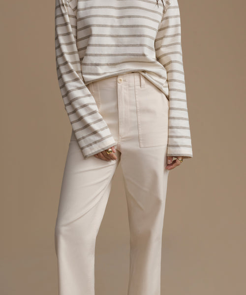 Person wearing a striped long-sleeve shirt and beige pants on a brown background