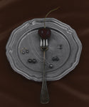 A silver fork with a dark cherry rests on a vintage metal plate, surrounded by Modern Elegance Jewelry, featuring the Medium Loren Pearl Studs and a necklace, all displayed on a deep brown fabric background.