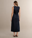 Woman stands with her back to the camera, wearing the sleeveless, ankle-length Blair Dress in dark navy linen and brown heeled sandals against a neutral beige background—an ideal choice to refresh your spring wardrobe.