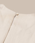 Close-up of the Blair Dress’s back neckline, showing a round button fastening at the top of a vertical seam. This light beige linen dress is perfect for your spring wardrobe, shown against a matching beige background.