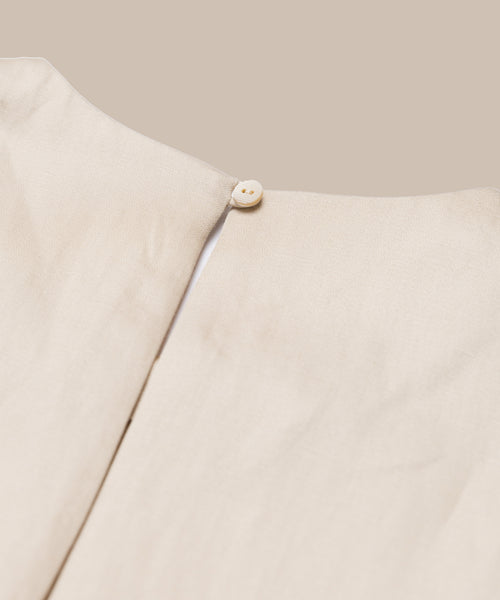 Close-up of the Blair Dress’s back neckline, showing a round button fastening at the top of a vertical seam. This light beige linen dress is perfect for your spring wardrobe, shown against a matching beige background.