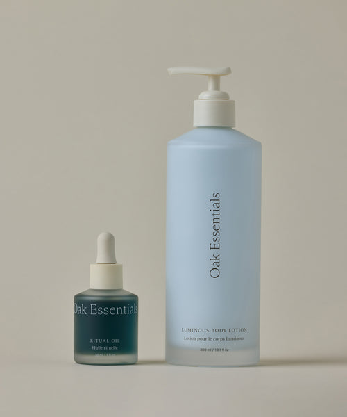 The Blue Tansy Bundle features two Oak Essentials hydrators: a small blue Ritual Oil dropper bottle with blue tansy and a large light blue Luminous Body Lotion pump bottle for dewy skin, set on a neutral background.