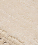 Close-up of a cream-colored textured fabric, bone in hue, with horizontal woven lines and fringe at the bottom edge. The soft, fluffy material suggests this is a Rug Swatch.