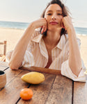 Woman wearing a stripe button up shirt at the beach. 