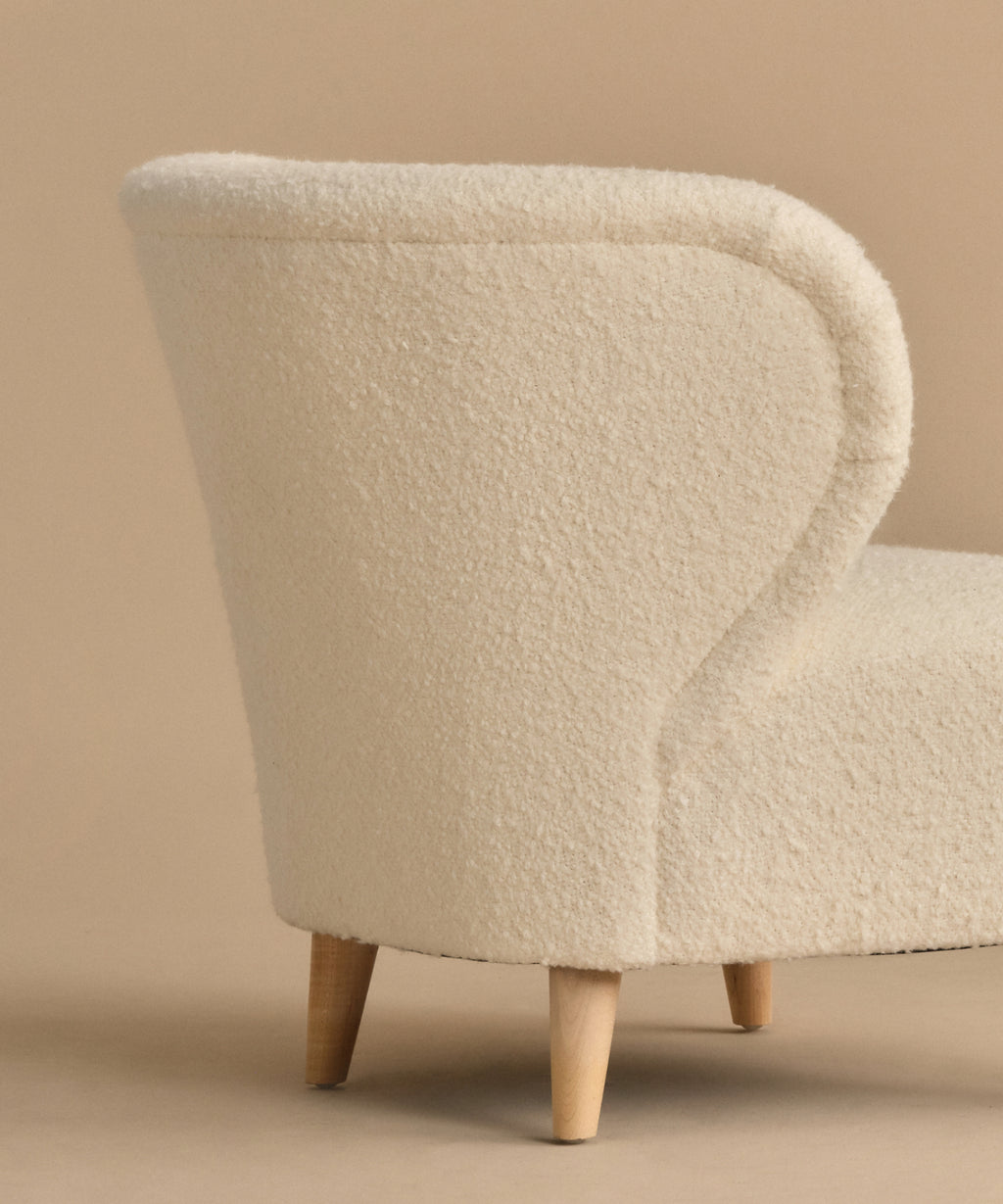 The Brentwood Chair features a modern curved backrest, ivory wool boucle upholstery, and light wooden legs, shown against a beige background.