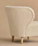 The Brentwood Chair features a modern curved backrest, ivory wool boucle upholstery, and light wooden legs, shown against a beige background.