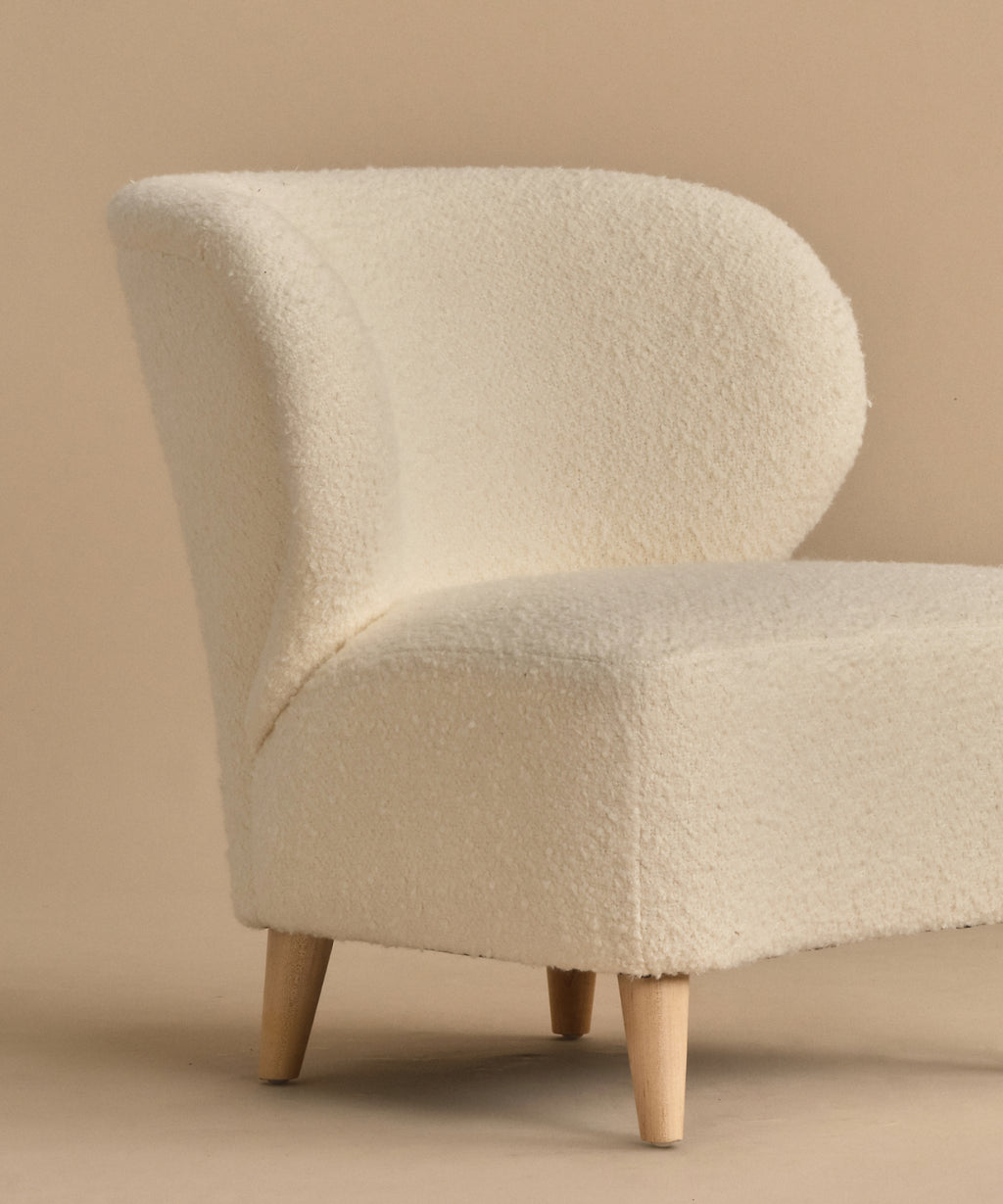 The Brentwood Chair features a curved backrest and soft ivory Belgian Wool Boucle upholstery, supported by four light wood legs, all showcased against a beige background.
