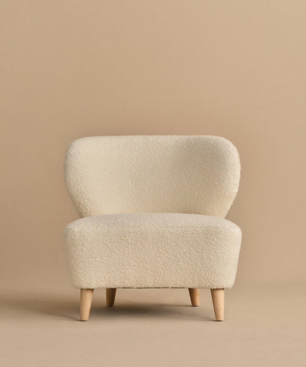 The Brentwood Chair is a modern piece, upholstered in ivory wool boucle with cream tones and light wood legs, shown against a plain beige background.