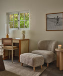 Living room with a sofa, ottoman, and a window with greenery outside.