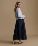 Woman wearing a light blue sweater and navy skirt on a beige background