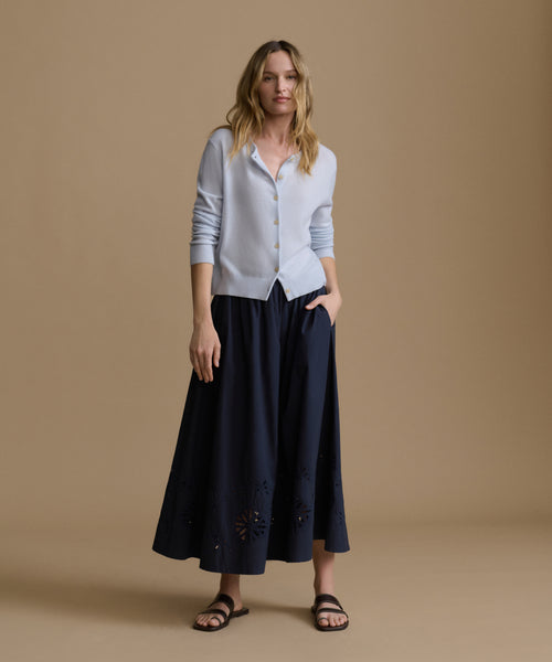 Woman wearing a light blue shirt and dark blue skirt against a beige background
