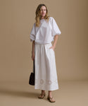 Woman wearing a white top and skirt with cut-out details on a beige background