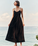Woman in a black dress standing by the ocean with a soft sky background