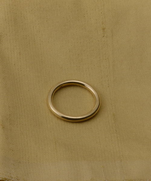 The Brook Gold Band, crafted in 14k gold, is displayed on a light tan fabric background with a subtle texture and minor stains.