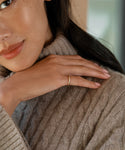 A woman in a beige cable-knit sweater gently rests her hand, showcasing the elegant Brook Gold Band in 14k gold, on her shoulder. Only the lower half of her face is visible, highlighting her smooth skin and subtle makeup.