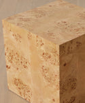 The Sur Side Table is a cube-shaped side table crafted from light mappa burlwood with a natural burled grain, shown on a light wooden floor.