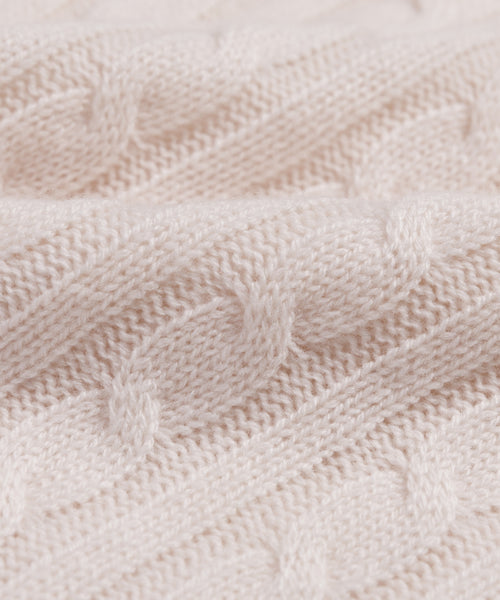Close-up of the Cable Nell Turtleneck, a soft, light beige sweater featuring a classic cable knit pattern, detailed texture, and subtle boxy silhouette with gentle folds.