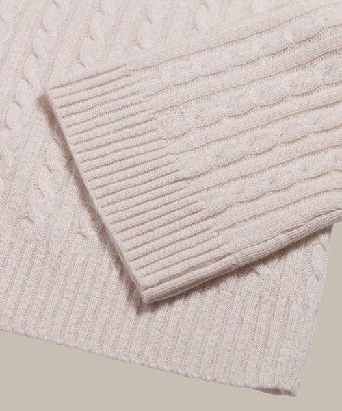 A close-up of the Cable Nell Turtleneck’s cream cable-knit sleeve over the body highlights ribbed cuffs, textured patterns, and its cozy boxy silhouette.