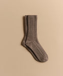 A pair of Cable Socks in ultra-stretchy, ribbed brown wool is neatly stacked on a light beige background.