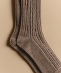 A close-up of Cable Socks in brown, featuring an ultra-stretchy ribbed knit pattern, laid flat on a beige background.