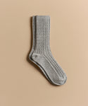 A pair of light gray Cable Socks, made from ultra-stretchy material, is laid flat on a neutral beige background—ideal for everyday wear.
