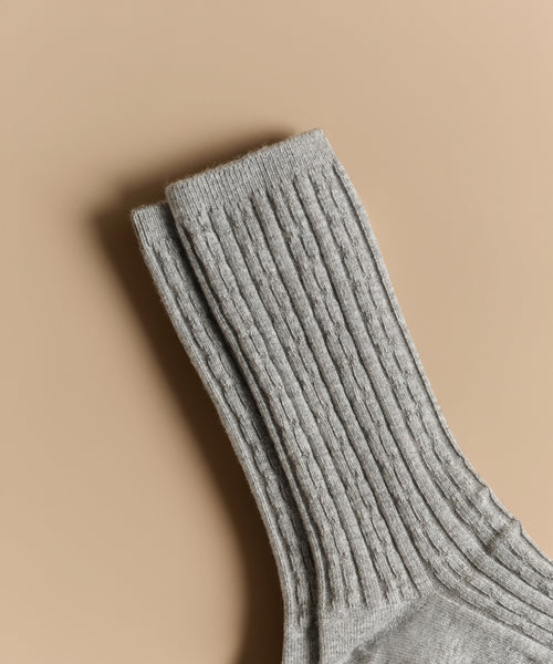 A close-up shows Cable Socks in light gray with ribbed texture on a beige background, ideal for everyday wear.
