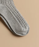 A close-up of Cable Socks in grey with a ribbed, textured knit pattern, ideal for everyday wear, shown lying flat on a beige surface.