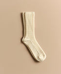 A cream-colored, ribbed Cable Sock is displayed flat on a beige background—ideal for everyday wear.