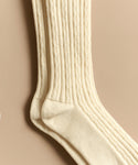 Cable Socks in a cream color feature a ribbed cable pattern and ultra-stretchy knit for comfortable everyday wear, displayed flat on a neutral beige background.