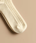 A close-up of cream-colored Cable Socks, featuring a ribbed texture and ultra-stretchy, soft material. The toe and foot sections are visible on a light beige surface—perfect for everyday wear.