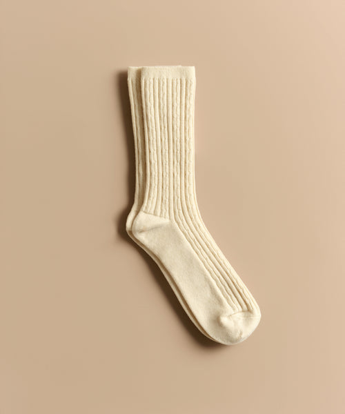 A cream-colored, ribbed Cable Sock is displayed flat on a beige background—ideal for everyday wear.