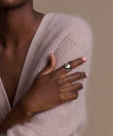A person with medium-dark skin crosses their arms against a neutral beige background, wearing a soft pale pink fuzzy sweater and the chunky Campbell Cigar Band on their left hand.