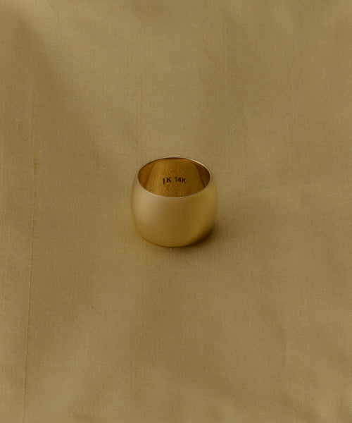 The Campbell Cigar Band, a wide 14k solid gold ring stamped with 14K inside, rests on smooth light tan fabric, capturing the timeless style of Jenni Kayne Jewelry.