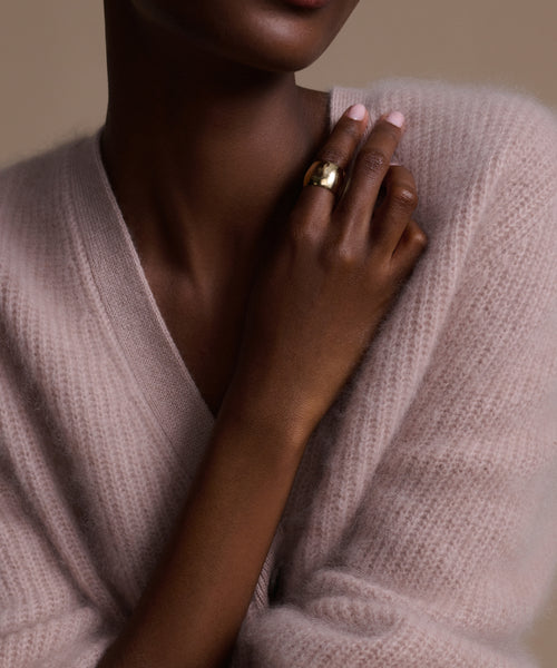 A person in a light pink fuzzy sweater holds their hand to their chest, showcasing the striking Campbell Cigar Band in 14k solid gold by Jenni Kayne Jewelry against a neutral background.