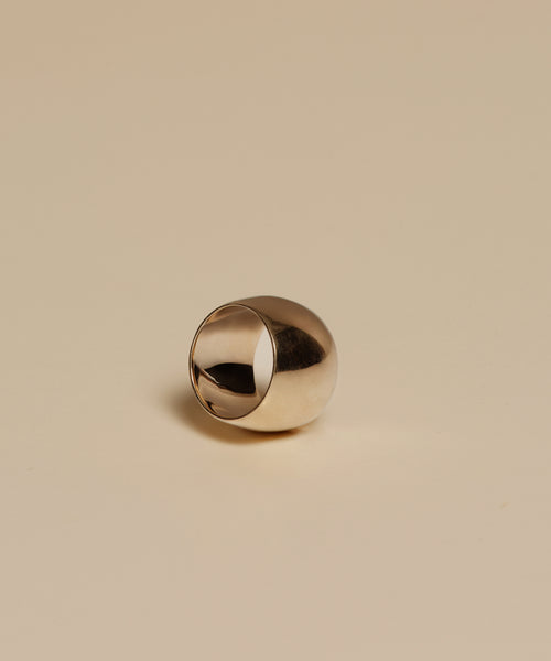 The Campbell Cigar Band, a shiny metallic dome-shaped ring, rests on a smooth beige surface under soft lighting with a minimalist background.