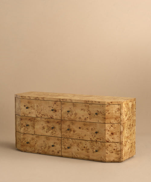 The Carbon Dresser features a light burlwood finish with natural, burled wood grain, six soft-close drawers with small round knobs, all set against a plain beige background.