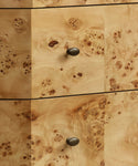 Close-up of a burl wood drawer front with two dark oval knobs, showing natural swirling grain and dark wood knots in light tan wood.