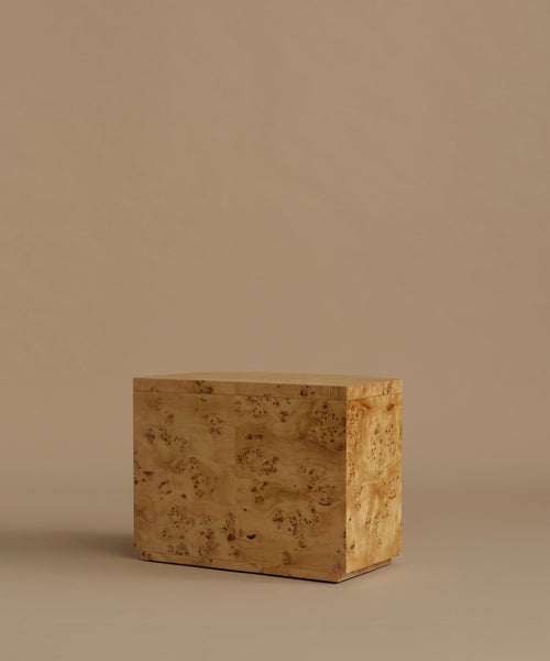A burlwood nightstand with drawers, featuring natural burl wood grain and small dark metal knobs, set against a solid beige background.