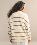 A person with long, curly hair faces away from the camera, modeling the Chloe Cardigan in ivory taupe stripe with white pants against a neutral backdrop—a stylish choice for warm-weather layering.