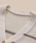 Close-up of the Chloe Cardigan, a cream knit sweater with an ivory taupe stripe V-neckline, showcasing its texture and stitching details—ideal for warm-weather wear and set against a beige backdrop.