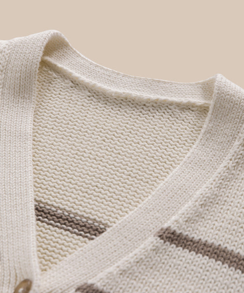 Close-up of the Chloe Cardigan, a cream knit sweater with an ivory taupe stripe V-neckline, showcasing its texture and stitching details—ideal for warm-weather wear and set against a beige backdrop.