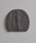The Cashmere Alpine Beanie, featuring a classic fisherman rib texture in gray, is displayed flat on a light, textured surface.
