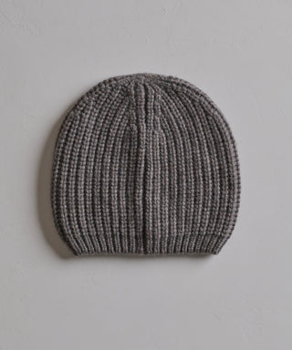 The Cashmere Alpine Beanie, featuring a classic fisherman rib texture in gray, is displayed flat on a light, textured surface.