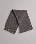 The Cashmere Alpine Scarf, featuring a chunky ribbed design in gray, is laid flat on a light gray surface.