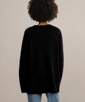 A person with curly hair, seen from behind against a plain light background, wears the Cashmere Amelia Crewneck in black paired with blue jeans.