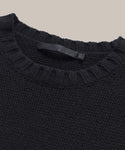 Close-up of the Cashmere Amelia Crewneck in black, featuring a ribbed crew neckline and an inner fabric label. Shown against a plain light beige background.