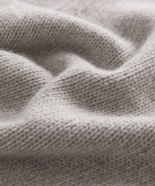 Close-up of soft, light gray knit fabric with a wavy texture and visible stitches, capturing the warmth and coziness of the Cashmere Amelia Crewneck sweater.