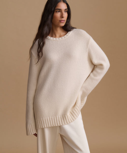 A woman wearing a cream-colored knit sweater and matching pants, photographed against a solid beige studio background.