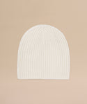 The Cashmere Beanie in ivory features a ribbed knit and lightweight cashmere blend, shown flat on a light beige background for an elegant look.