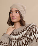 A woman wearing a Cashmere Beanie and a beige and brown patterned sweater looks to the side against a matching beige background.